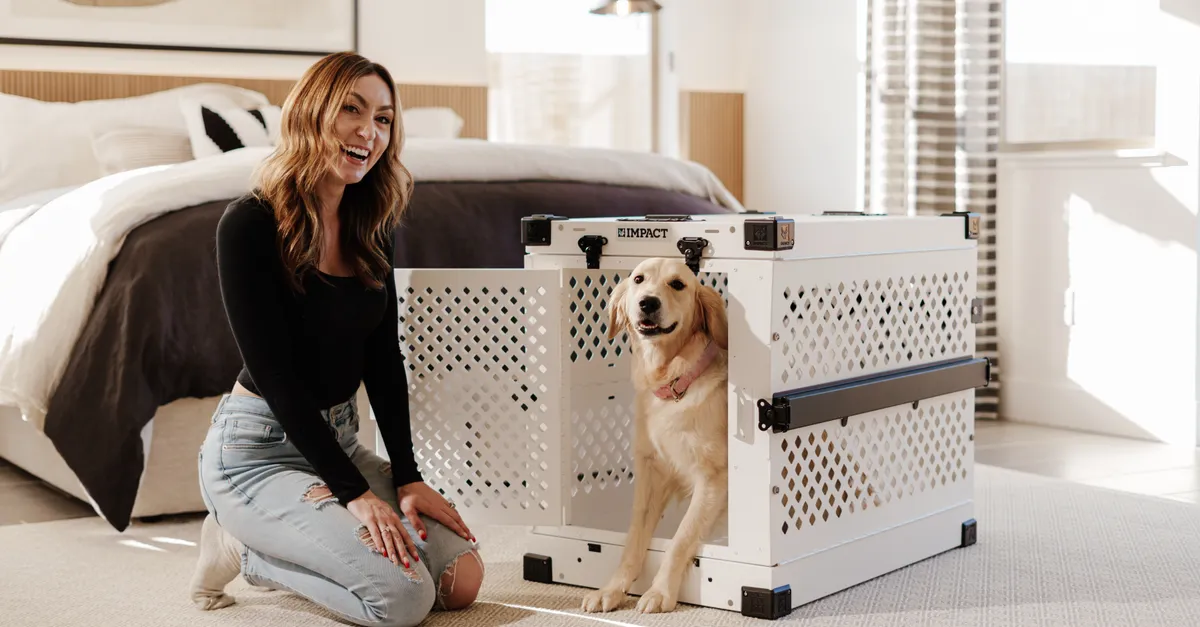 A cheerful woman poses with a golden retriever next to a premium dog crate in a stylish bedroom.