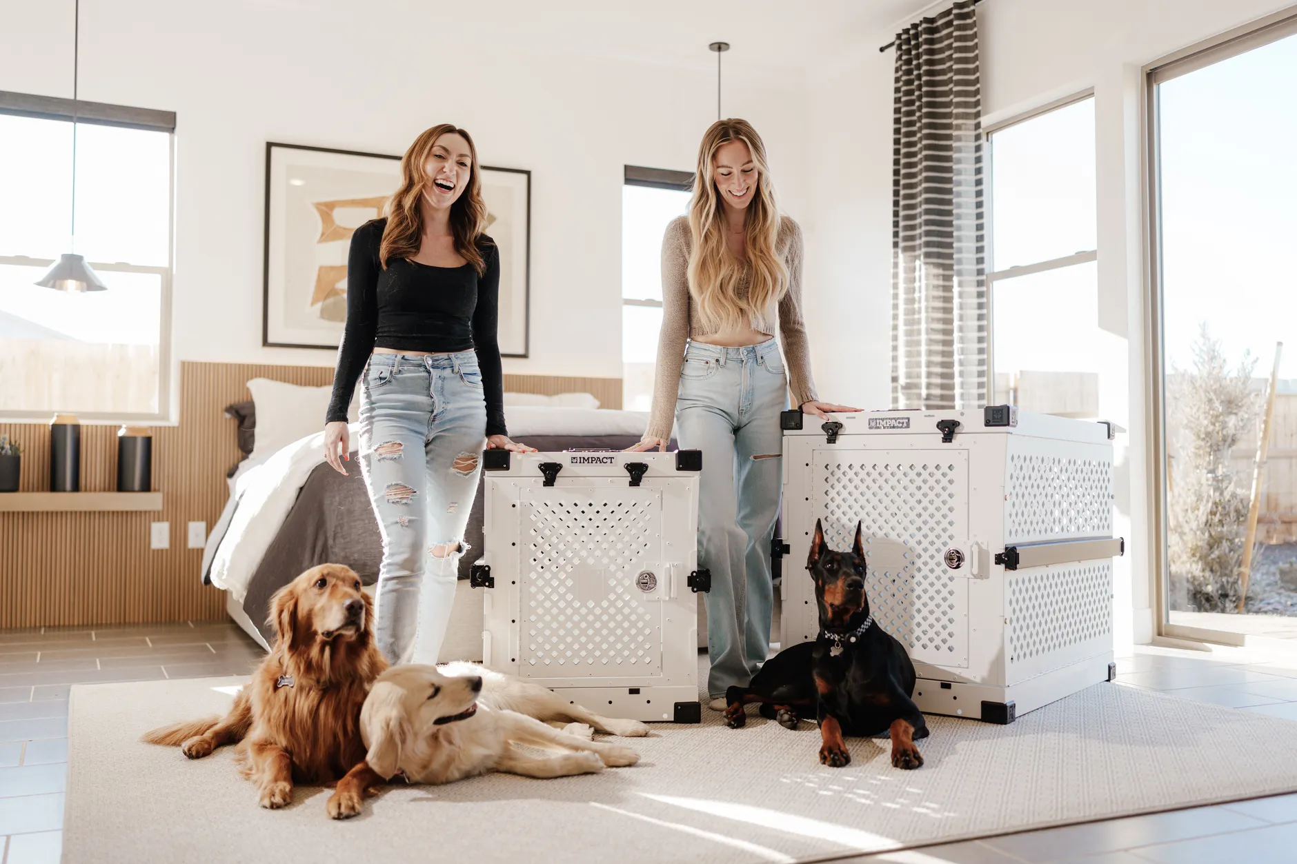 Two women and their dogs enjoying a sunny indoor bedroom with stylish crates.
