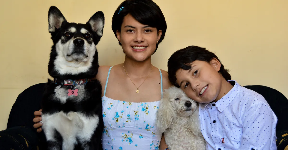 Happy siblings smiling with their dogs, creating a warm family moment indoors.