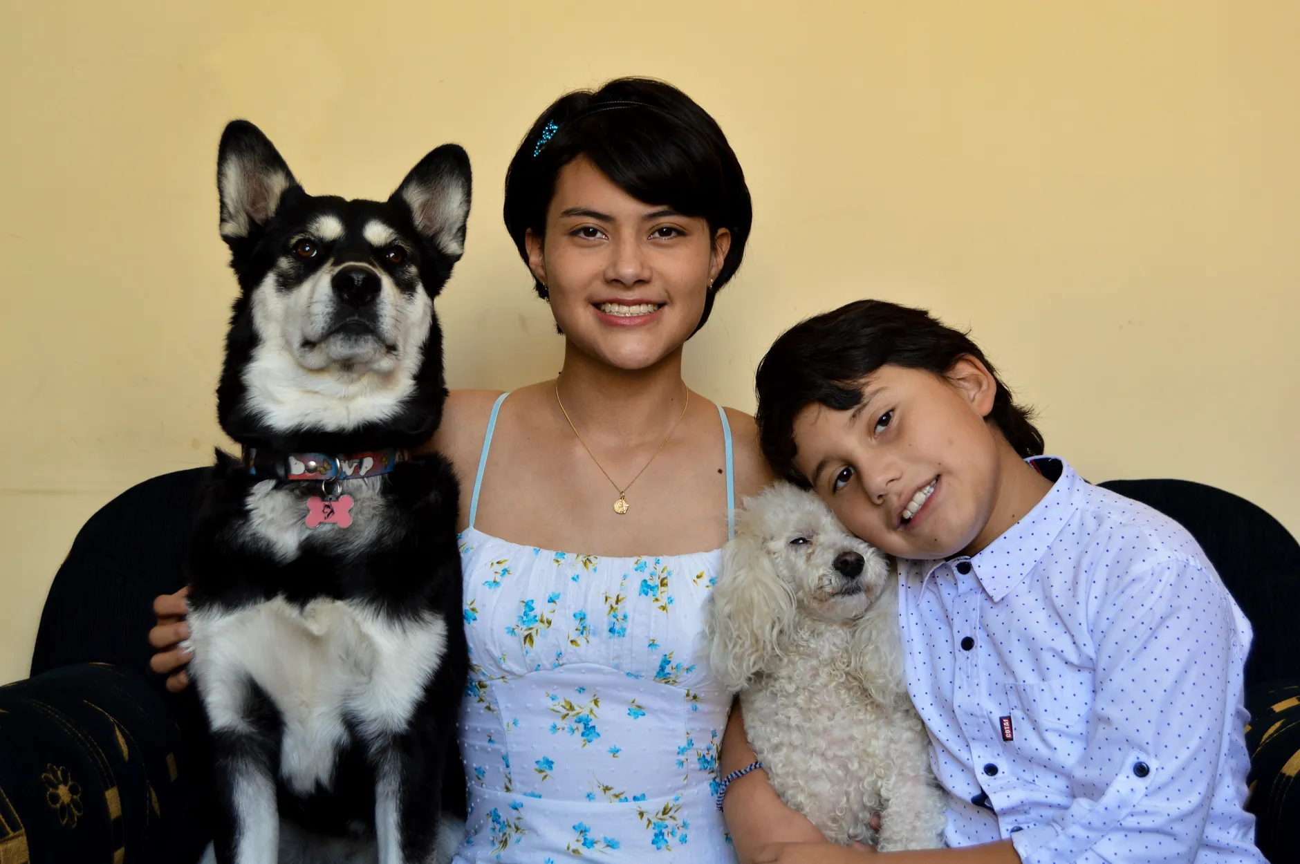 Happy siblings smiling with their dogs, creating a warm family moment indoors.