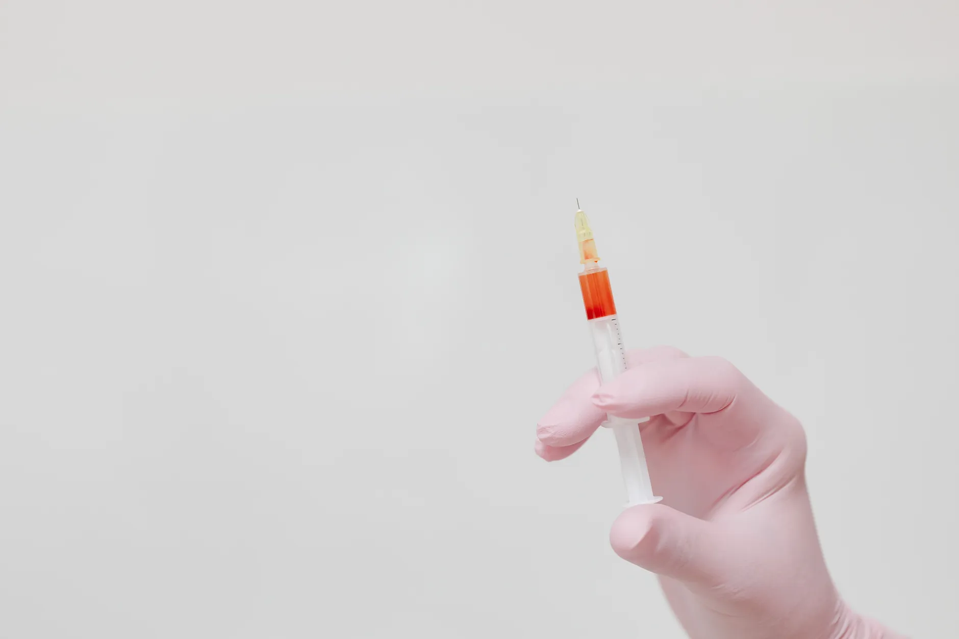 A gloved hand holding a syringe against a neutral background.
